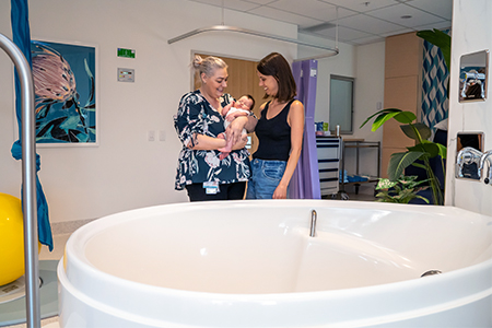 Two women stand beside a large bath in the Family Birthing Centre