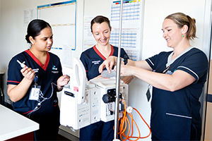 A female nurses demonstrates to two female graduate nurses how to set up an item of medical equipment .