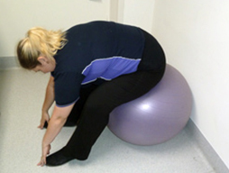 Woman sitting on fitball leaning forward with her hands reaching towards her toes