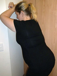 A pregnant woman leans into a wall in front of her, with her forearms raised to head height to support her