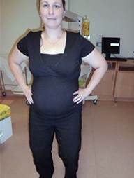 A pregnant woman stands with her feet hip width apart and her hands on her hips. Her knees are bent slightly.
