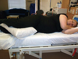 A pregnant woman lies on her side on a hospital ed. A pillow is placed between her legs.