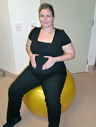 A woman sits on a fitball and places her hands on either side of her stomach.