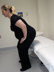 A woman moves to a standing position from a bed with her hands on her thighs.