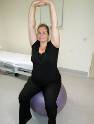 Woman sitting on a fitball with her arms reaching above her head with her fingers interlaced