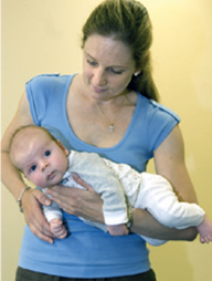 A woman holds carries a baby face down on her forearm with the baby’s head at the woman’s hand.