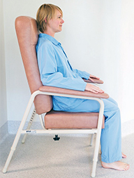 A woman sits in a chair with a high back. Her feet are on the floor and her hips and keens at a ninety-degree angle.