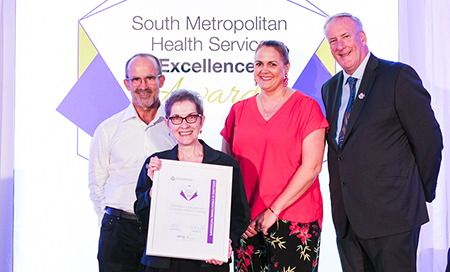 Two men and two women stand in front of a banner that reads South Metropolitan Health Service Excellence Awards. One woman holds a framed certificate.